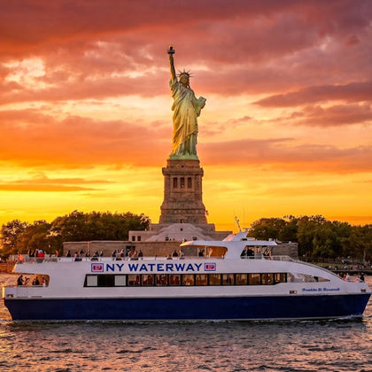 A ferry labeled 'NY Waterway' passes in front of the Statue of Liberty during a vibrant sunset.
