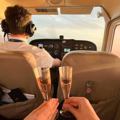 A pilot flying a small aircraft with two hands in the foreground clinking champagne glasses.
