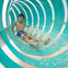 A child sliding down a colorful water slide with flowing water, wearing swimwear and smiling.