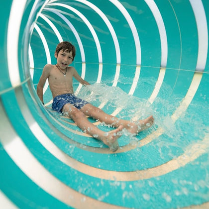 A child sliding down a colorful water slide with flowing water, wearing swimwear and smiling.