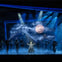 A theatrical performance with a moonlit backdrop, fog effects, and actors in dark costumes on stage under dramatic lighting.