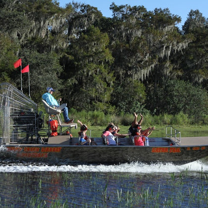 A group of people enjoying an airboat ride through a marshy area with dense trees in the background.