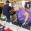 A woman in a purple shirt examines a dining table set with plates, glasses, and a centerpiece, with others in the background.
