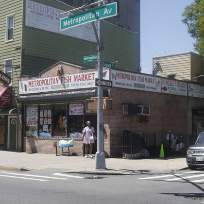 A street corner with a fish market and a person standing outside. A Metropolitan Av street sign is visible overhead.