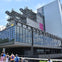 People walking near a modern glass building with multiple floors and observation decks under a clear sky.