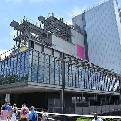 People walking near a modern glass building with multiple floors and observation decks under a clear sky.
