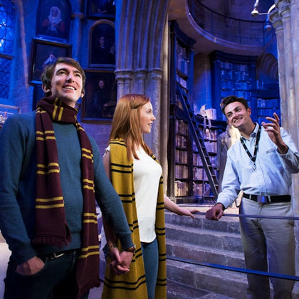 A guide explains a library exhibit to a couple, who are holding hands and wearing matching scarves.
