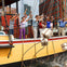 A group of people on a ship deck throwing packages overboard into the water, with a cityscape visible in the background.