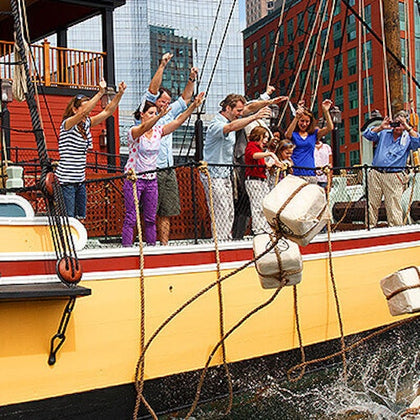 A group of people on a ship deck throwing packages overboard into the water, with a cityscape visible in the background.