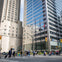 A busy city intersection with pedestrians crossing and tall buildings in the background.