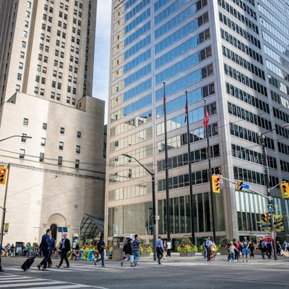 A busy city intersection with pedestrians crossing and tall buildings in the background.