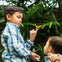 Two children interacting with a butterfly in an outdoor setting with lush greenery.