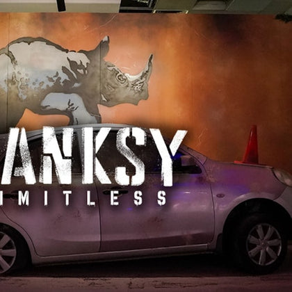 A silver car parked indoors with a painted rhino mural in the background and the text 'BANKSY LIMITLESS' overlaid.