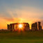 Stonehenge at sunset with the sun perfectly aligned between two stones, casting vibrant orange and yellow hues.
