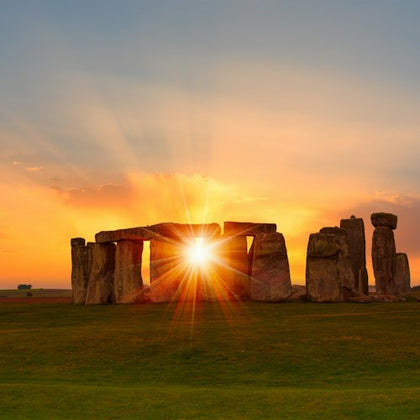 Stonehenge at sunset with the sun perfectly aligned between two stones, casting vibrant orange and yellow hues.