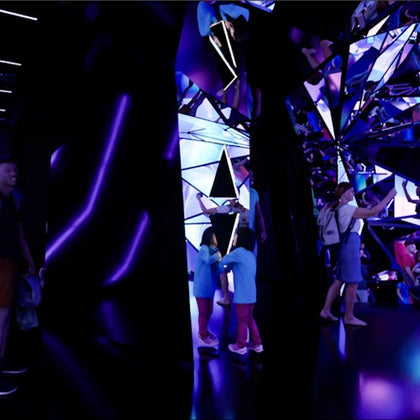 A mirrored, futuristic space with purple lighting, showing people exploring and interacting with reflective surfaces.