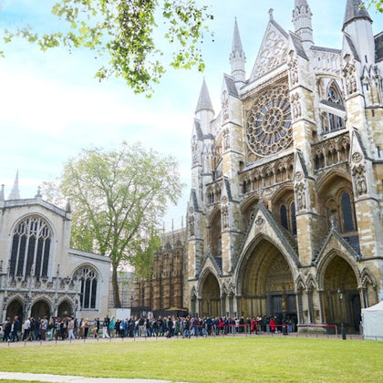 A crowd of people in line outside a large Gothic cathedral with intricate architecture on a sunny day.