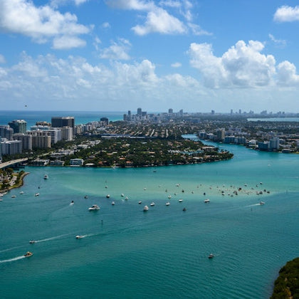 A coastal cityscape with buildings, waterways, and numerous boats in the water under a partly cloudy sky.