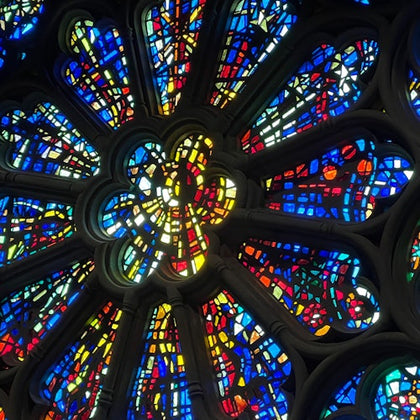 A close-up view of a stained glass rose window with colorful, symmetrical patterns illuminated by light.