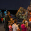 A group of children and an adult observe a spacecraft interior on display. Astronaut mannequins are visible in the background.