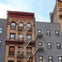 A section of a city building with fire escapes on the facade. The structure has a mix of brick and painted surfaces.
