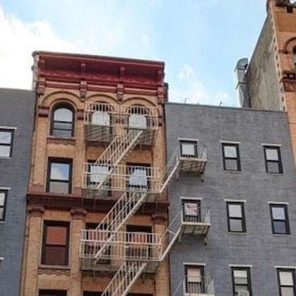 A section of a city building with fire escapes on the facade. The structure has a mix of brick and painted surfaces.