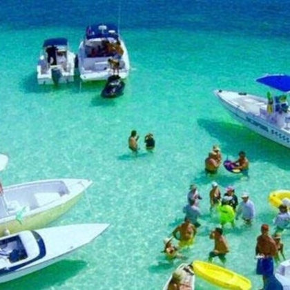 Crystal-clear waters, boats gently floating, and people wading in shallow bliss—an idyllic scene of serene relaxation