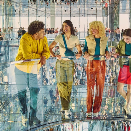 A group of four people standing on a glass floor in a mirrored room, conversing and enjoying the surroundings.