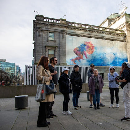 A group of people gathered in front of an old building with a large mural depicting a person swimming underwater.