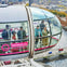 People inside a glass capsule of the London Eye, overlooking the River Thames and Westminster Bridge on a sunny day.