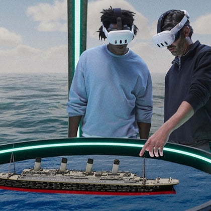 Two people wearing VR headsets interact with a 3D model of a ship floating in a virtual environment above the ocean.