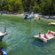 Boat anchored by the island's shore, people on large rafts enjoying seaside leisure—an idyllic water escapade moment.