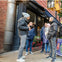 A group of five people, dressed in winter clothing, stands outside a building on a city sidewalk.
