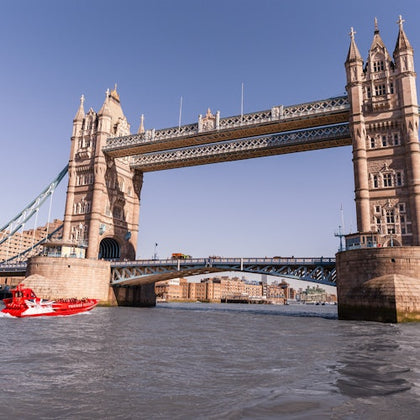 Tower Bridge over the River Thames on a clear day, with a red speedboat in the foreground.