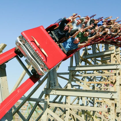 A red roller coaster shaped like a classic car with passengers leaning and holding their hands up, on a wooden structure.