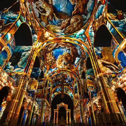 A church interior illuminated with colorful projection art featuring celestial and religious themes on its walls and ceiling.