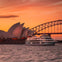A white boat on the water near the Sydney Opera House and Sydney Harbour Bridge during sunset.
