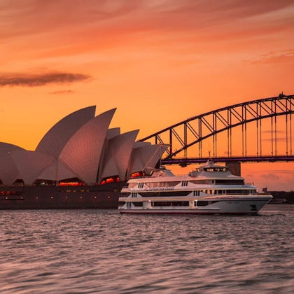 A white boat on the water near the Sydney Opera House and Sydney Harbour Bridge during sunset.