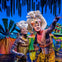 Performers in colorful costumes and lion masks on stage with a jungle-themed backdrop.