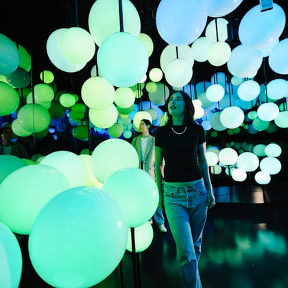 A woman walking through a room filled with glowing green and blue spherical lights.