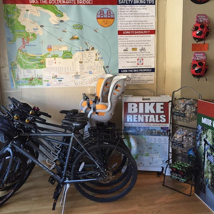 A bike rental shop with bikes, a child seat, a map, safety tips, and Muir Woods promotional materials displayed.