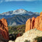A scenic view of red rock formations in a desert landscape with a snow-capped mountain range in the background under a blue sky.