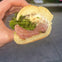 A close-up of a hand holding a sandwich with layers of meat, lettuce, and cheese on a sliced bread roll.