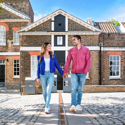 A couple holds hands while walking on a cobblestone path in front of a historic brick building under a clear blue sky.