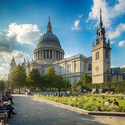 A large cathedral with a dome and towers surrounded by a park with benches, trees, and people enjoying the scenery.