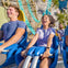 Two people smiling and screaming with excitement while riding a roller coaster against a sunny backdrop.