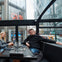 Two people sitting in a glass-enclosed restaurant with city buildings in the background, including a CVS store.