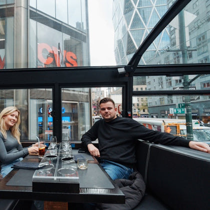 Two people sitting in a glass-enclosed restaurant with city buildings in the background, including a CVS store.