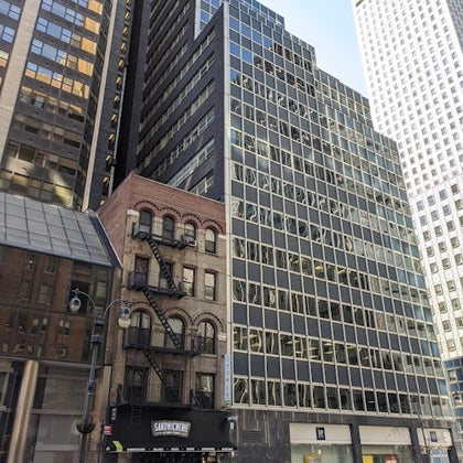 A city scene featuring a mix of architectural styles, including a small brick building with fire escapes next to tall modern skyscrapers.