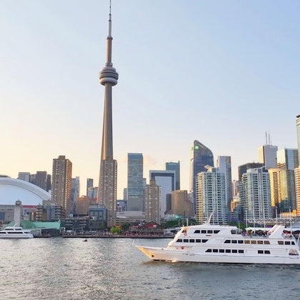 A cityscape view of Toronto with the CN Tower, skyscrapers, and boats on the waterfront under a clear sky.